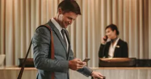 Homem de terno com bolsa no ombro direito na recepção de um hotel onde será feita a hospedagem de sua viagem a trabalho