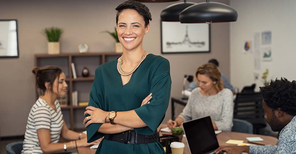 Mulher negra executiva com os braços cruzados e olhar confiante para denotar o empoderamento feminino no mercado de trabalho